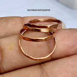 Puede incluir: Un conjunto de tres anillos de metal fino de color cobre con una textura martillada e irregular. Los anillos están apilados, mostrando un acabado metálico cálido. El texto SILVERLEGANCEJAIPUR es visible en la parte superior.