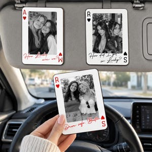 Könnte beinhalten: Drei rechteckige Sonnenblenden-Clips im Design von Spielkarten mit Schwarz-Weiß-Fotos von zwei Personen. Die Karten zeigen rote Herzsymbole, die Buchstaben A, R und S sowie den Text How Lucky are we?, How did I get so Lucky? und Drive safe. Bestie.
