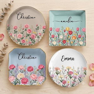 May include: Four ceramic trinket dishes with gold-toned rims. Two are round and two are square. Each dish features a unique floral pattern in pink, yellow, and white, and is personalised with the names Christine, Amelia, or Emma in black script.