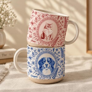 May include: Two stacked ceramic mugs with a cream-colored base. The top mug features a red floral pattern and a portrait of a cat with the name Oreo. The bottom mug features a blue floral pattern and a portrait of a dog with the name Cooper.