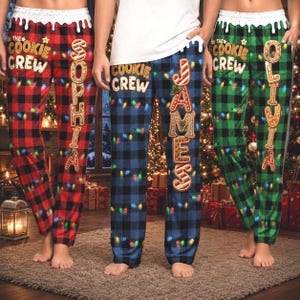Peut inclure: Trois pantalons de pyjama à carreaux rouges, bleus et verts, dotés d'une ceinture blanche avec un motif de glaçage dégoulinant, l'inscription Cookie Crew et un prénom vertical en lettres style pain d'épices avec des lumières de Noël.