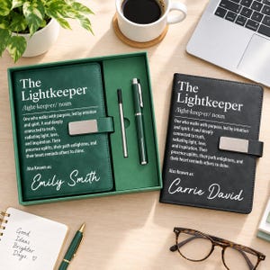 May include: A green notebook with a matching pen in a gift box and a black notebook, both featuring the text The Lightkeeper, a definition, and personalised names. The green notebook is labelled Emily Smith and the black one Carrie David.