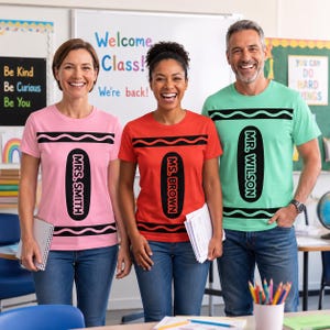 May include: Three short-sleeved t-shirts designed to look like crayons. The pink shirt says MRS. SMITH, the red shirt says MS. BROWN, and the light green shirt says MR. WILSON. Each shirt features black wavy lines and a black oval label design.