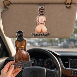 Könnte beinhalten: Zwei Acryl-Sonnenblenden-Ornamente für Autos mit Illustrationen von Figuren von hinten. Eine Figur hat dunkles Haar und ein gelbes Oberteil, die andere einen braunen Dutt und ein rotes Oberteil. Der Text lautet: "You are my favorite pain in the ass" und "I love you with all my butt, I would say my heart, but my butt is bigger."