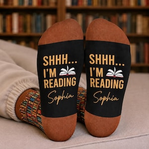 May include: A pair of socks with brown heels and toes, featuring a black midsection printed with the text SHHH... I'M READING, an illustration of an open book, and the name Sophia in a cursive script. The ankle area displays a colourful book pattern.