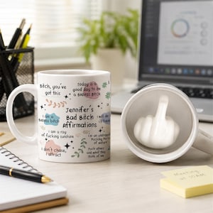 May include: A white ceramic mug featuring the text Jennifer's Bad Bitch Affirmations and various phrases in black font with colourful abstract shapes. A second view shows the interior of the mug with a white sculpted hand making a middle finger gesture.