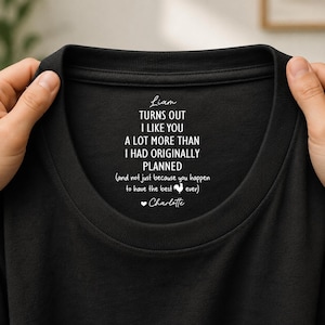 May include: A black t-shirt featuring white printed text on the inner neckline that reads: Liam, TURNS OUT I LIKE YOU A LOT MORE THAN I HAD ORIGINALLY PLANNED (and not just because you happen to have the best rooster ever) Charlotte.