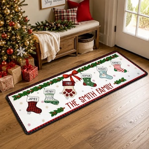 May include: A rectangular floor mat with a white background and a red and black buffalo plaid border. The design features a green holly garland with hanging Christmas stockings labelled James, Henry, Milo, Sophia, Susan, and Daniel, with the text THE SMITH FAMILY.