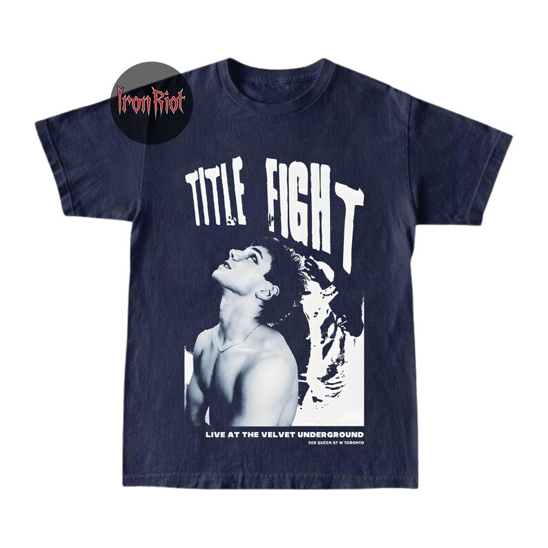 Puede incluir: Camiseta azul marino con un gr&aacute;fico en blanco y negro. El gr&aacute;fico presenta el texto "TITLE FIGHT" sobre una imagen de una persona mirando hacia arriba. Debajo de la imagen, el texto dice "LIVE AT THE VELVET UNDERGROUND" y "508 QUEEN ST W TORONTO".