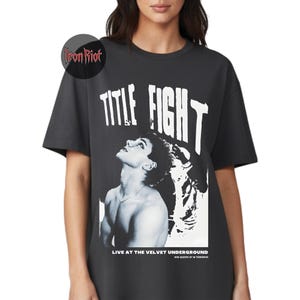 Puede incluir: Camiseta gris oscuro con el texto "TITLE FIGHT" en letras blancas grandes. Debajo, una imagen en blanco y negro de una persona mirando hacia arriba. El texto "LIVE AT THE VELVET UNDERGROUND" est&aacute; impreso en la parte inferior.