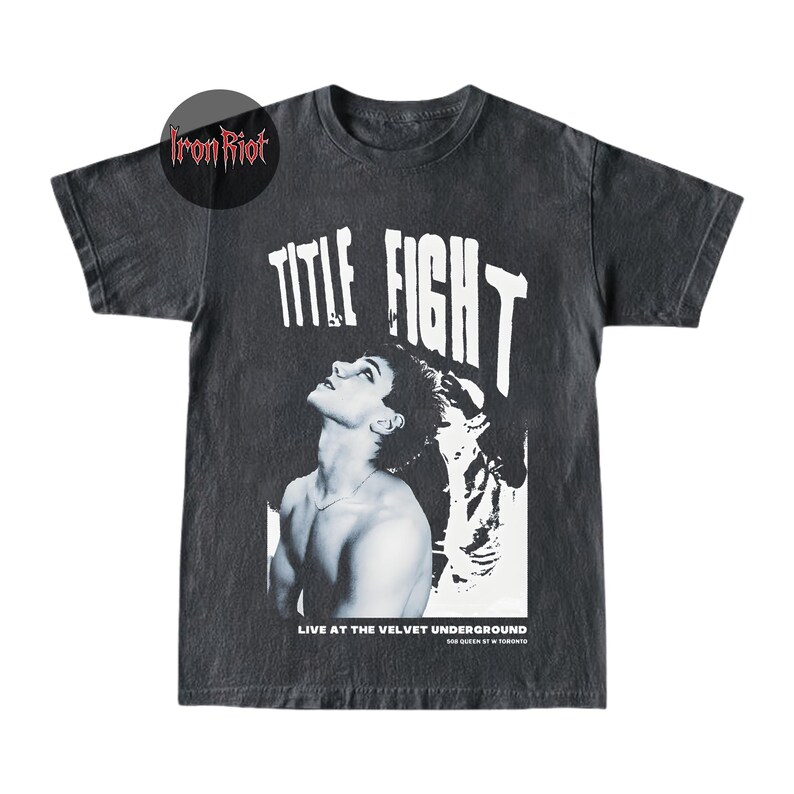 Puede incluir: Camiseta gris oscuro con un gr&aacute;fico en blanco y negro de una persona mirando hacia arriba, con las palabras "TITLE FIGHT" en letras blancas grandes. Debajo del gr&aacute;fico, el texto dice "LIVE AT THE VELVET UNDERGROUND". La camiseta tiene un aspecto vintage.