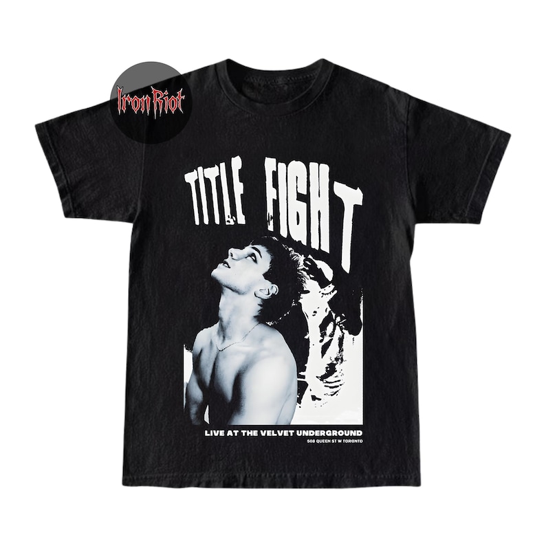 Puede incluir: Camiseta negra con un dise&ntilde;o gr&aacute;fico que presenta el texto "TITLE FIGHT" en letras blancas grandes. El dise&ntilde;o incluye una imagen en blanco y negro de una persona mirando hacia arriba. El texto "LIVE AT THE VELVET UNDERGROUND" tambi&eacute;n est&aacute; impreso en la camiseta.