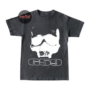 Op de afbeelding: Donkergrijs t-shirt met een witte schedelafbeelding en de tekst "G59". Het t-shirt heeft een vintage, verweerde uitstraling. Het merklogo "Iron Riot" is zichtbaar in de linkerbovenhoek.