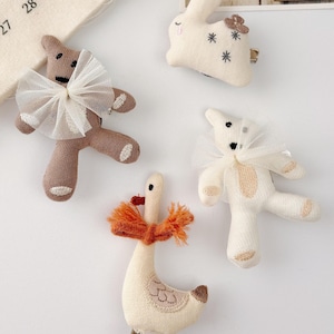 Puede incluir: Cuatro pinzas para el pelo de tela con forma de oso de peluche, conejo y ganso. Los osos de peluche tienen lazos de tul blanco. El conejo tiene estrellas bordadas y una flor. El ganso lleva una bufanda naranja. Estas pinzas son ideales para niños.