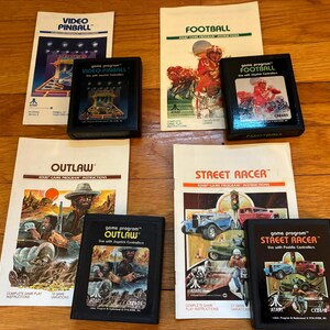 May include: A collection of Atari game cartridges and instruction manuals. Games include "Video Pinball", "Football", "Outlaw", and "Street Racer". The cartridges are black, and the manuals feature colorful illustrations.