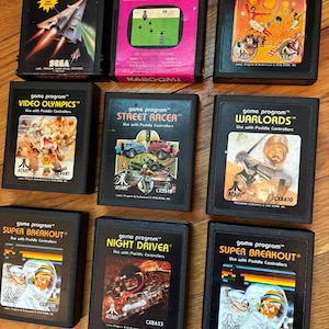 May include: A collection of nine vintage Atari game cartridges, including titles like "Kaboom!", "Circus Atari", and "Super Breakout." The cartridges feature colorful game art and text labels, showcasing classic gaming graphics.