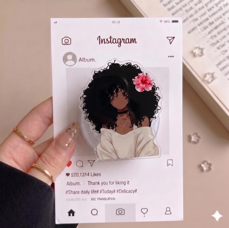 May include: A clear acrylic phone stand designed as an Instagram post. It features a black woman with curly hair, a pink flower, and a white top. The stand has Instagram interface elements.