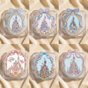 May include: Six clear, square cases with decorative castle designs. Each case features a different castle illustration within an oval or rounded frame, adorned with bows and ribbons in pastel colors. The cases are arranged on a textured, light-colored surface.