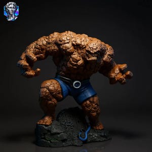 May include: A detailed figurine of The Thing from the Fantastic Four. The figure is primarily brown with a rocky texture, wearing blue shorts. It stands on a stone base with a blue cable detail, posed in a powerful stance.
