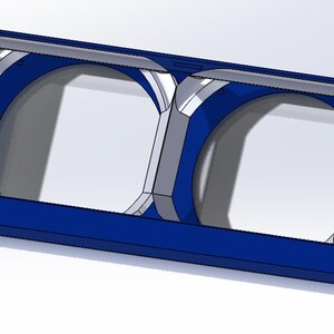 Puede incluir: Un marco rectangular azul con dos aberturas circulares. El marco tiene un diseño geométrico con detalles en gris y blanco. El objeto parece ser un modelo 3D o un componente de una estructura más grande.