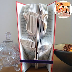 May include: A book with pages folded into the shape of a rose. The book is red and has a purple ribbon around it. The text "Pattern Only" is visible in the upper right corner of the image.