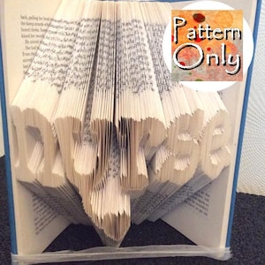 May include: A book art pattern for a 3D folded book sculpture of the word "DUPSE". The pattern is printed on a white background with colorful watercolor splatters. The text "Pattern Only" is printed in white on a circle with a colorful watercolor background.