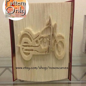 May include: A book folded into the shape of a motorcycle. The book is made of white paper and has a red spine. The motorcycle is in a neutral color and is facing the right side of the image. The text "www.etsy.com/shop/nosoxcarves" is printed on the bottom of the book.