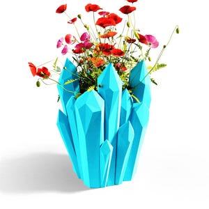 May include: A bright cyan, geometric, crystal-shaped vase holding a vibrant arrangement of red and pink poppy flowers with green stems and leaves. The vase features sharp, angular facets that mimic the appearance of a cluster of natural crystals.