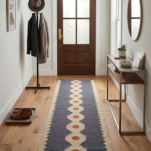 Peut inclure: Un couloir avec une porte en bois foncé, un tapis de couloir à motifs et un porte-manteau. Le tapis de couloir est bleu avec un motif répétitif de formes géométriques orange et crème. Un chapeau marron et des manteaux sont suspendus au porte-manteau.
