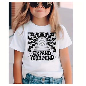 May include: White t-shirt featuring a black and white graphic of an eye within a triangle, surrounded by a wavy pattern. The text "EXPAND YOUR MIND" is below the graphic. The shirt is worn by a person wearing sunglasses.