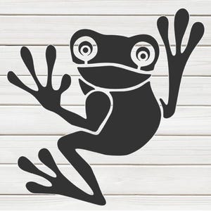 May include: A black frog silhouette with large eyes and outstretched limbs. The frog is depicted in a stylized, minimalist design, set against a white wooden plank background. The frog's pose suggests movement.