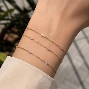 May include: Three delicate gold chain bracelets, each featuring small, evenly spaced clear stones. The thin, polished gold links create a layered look, with the sparkling stones catching the light along the length of each individual bracelet chain.