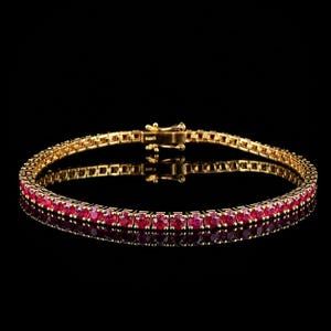May include: A gold tennis bracelet featuring a continuous row of round, vibrant red rubies set in individual gold prongs. The bracelet includes a secure box clasp mechanism at the centre, showcasing a polished gold finish throughout the design.