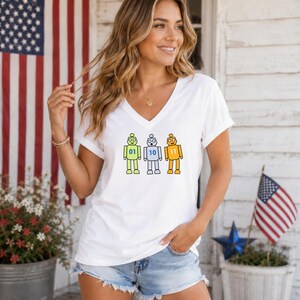 May include: A white V-neck t-shirt featuring a graphic of three cartoon robots in light green, light blue, and orange. Each robot has a binary number on its chest: 01 on the green robot, 10 on the blue robot, and 11 on the orange robot.