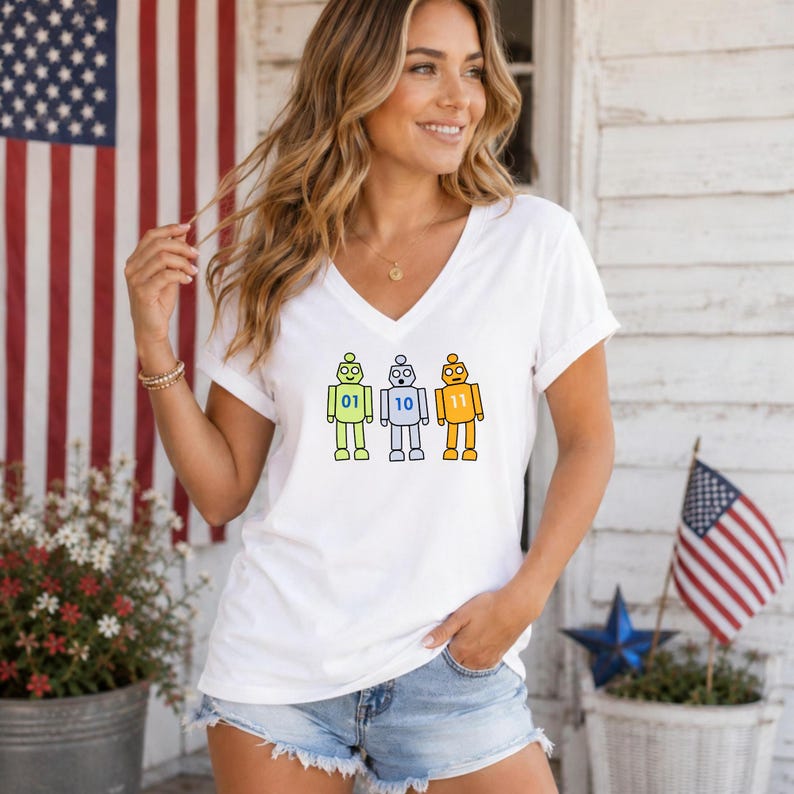 May include: A white V-neck t-shirt featuring a graphic of three cartoon robots in light green, light blue, and orange. Each robot has a binary number on its chest: 01 on the green robot, 10 on the blue robot, and 11 on the orange robot.