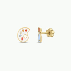 May include: A pair of gold-colored earrings. One earring is shaped like a painter's palette with colorful paint splotches. The other earring is a paintbrush with a flower-shaped backing. The earrings are set against a white background.