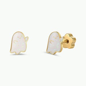 May include: A pair of stud earrings shaped like ghosts with gold-toned metal edges and a white enamel center featuring iridescent glitter flecks. The earrings include a flower-shaped backing mechanism visible on the side of one ghost stud.