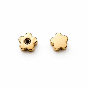 May include: Two gold-colored flower-shaped earrings. One earring has a small hole in the center. The earrings are set against a white background. The earrings have a smooth, polished finish.