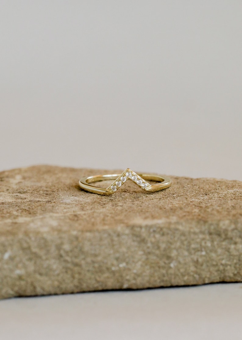 Puede incluir: Un anillo de oro con un dise&ntilde;o de chevron engastado con peque&ntilde;as piedras transparentes.