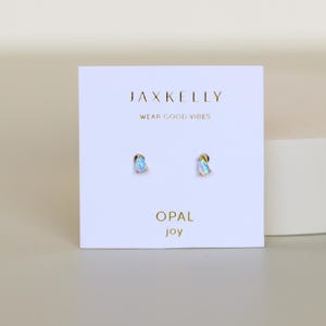 May include: A pair of opal stud earrings on a white card. The card has the text "JAXKELLY" at the top, with "WEAR GOOD VIBES" below it. The word "OPAL" and the word "joy" are at the bottom of the card.