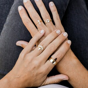 Puede incluir: Una mano lleva cuatro anillos de oro con diferentes piedras preciosas. Los anillos est&aacute;n en el &iacute;ndice, medio, anular y me&ntilde;ique. Las piedras preciosas son un cristal transparente, un peque&ntilde;o diamante, un grupo de peque&ntilde;os diamantes y una piedra negra.