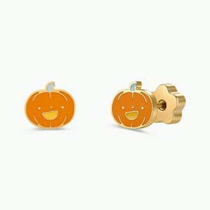 May include: A pair of stud earrings featuring a gold-toned pumpkin design with orange enamel filling. Each pumpkin has a smiling face with two small eyes and a wide mouth. The earrings include a flower-shaped backing and a post for secure attachment.