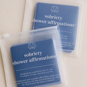 May include: A set of blue affirmation cards in a clear plastic bag. The cards feature a white lotus flower and the text "sobriety shower affirmations". The cards are designed to be used as a tool for recovery.