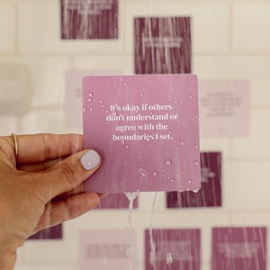 May include: A pink affirmation card with the text "It's okay if others don't understand or agree with the boundaries I set." The card is wet and has water droplets on it.
