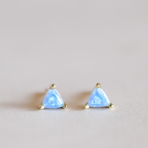 May include: A pair of gold triangle stud earrings with light blue opal stones.