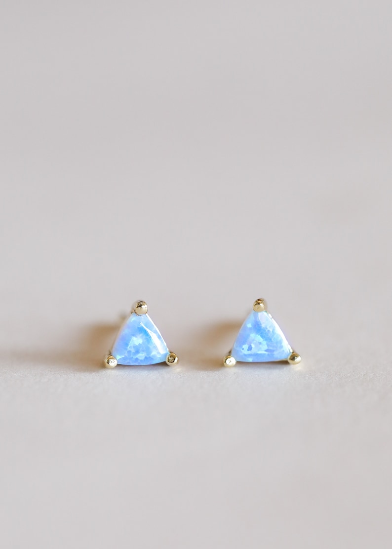 May include: A pair of gold triangle stud earrings with light blue opal stones.