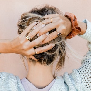 Puede incluir: Una mujer con cabello rubio que lleva un su&eacute;ter azul claro y varios anillos de oro en los dedos.