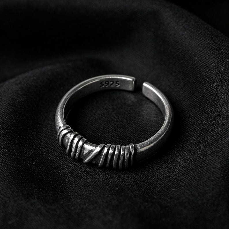 Peut inclure: Une bague ouverte de couleur argent&eacute;e pr&eacute;sentant un anneau textur&eacute; avec une s&eacute;rie de d&eacute;tails ressemblant &agrave; du fil enroul&eacute; sur le devant. L'int&eacute;rieur de l'anneau est clairement marqu&eacute; du texte S925, indiquant la composition de ce bijou r&eacute;glable.