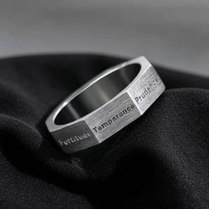 Peut inclure: Une bague en m&eacute;tal argent&eacute; avec une bande ext&eacute;rieure hexagonale au fini bross&eacute;. Les surfaces plates de la bague sont grav&eacute;es des mots Fortitude, Temperance et Prudence dans une police sans empattement, cr&eacute;ant un aspect g&eacute;om&eacute;trique distinct.