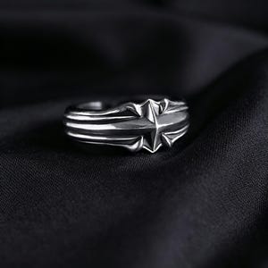 Peut inclure: Une bague en m&eacute;tal argent&eacute; pr&eacute;sentant un motif d'&eacute;toile &agrave; quatre branches pro&eacute;minent au centre. L'anneau est caract&eacute;ris&eacute; par des cr&ecirc;tes parall&egrave;les en relief qui s'&eacute;tendent horizontalement depuis le motif central, cr&eacute;ant un aspect structur&eacute;.